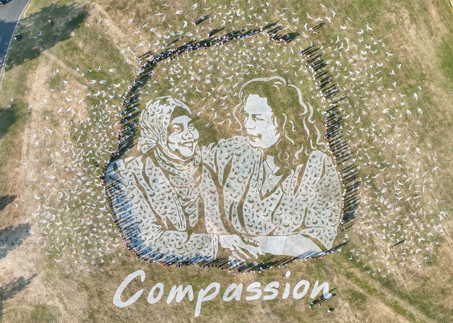 Stencilled giant land art of two women holding each other with the word compassion stencilled underneath